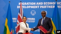 Sekretarja e Brendshme britanike Priti Patel, shtrëngon duart me Ministrin e Jashtëm të Ruandas, Vincent Biruta, pasi nënshkruan marrëveshjen që dy vendet e përshkruan si "një partneritet për zhvillimin ekonomik" (Kigali, Ruanda, 14 prill 2022)