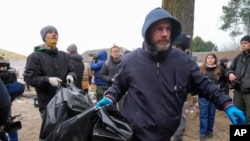 Policët mbartin kufomën e një civili të gjendur në Bucha (5 prill 2022)