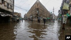 FILE - People wade through a flooded road after heavy rains, in Karachi, Pakistan, July 25, 2022.