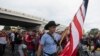 Yon migran pote drapo Ameriken an pandan lap rale yon malet nan mitan yon karavan migran kap kite Tapachula nan eta Chiapas, Meksik, bone 6 Jyen 2022. 