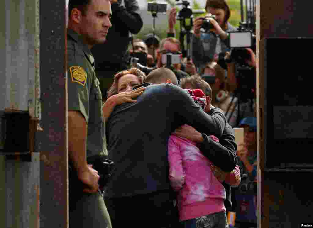 U.S. Border patrol agents stands at an open gate on the fence along the Mexico border as Adrian Gonzalez-Morales and his daughter Aileen hug his parents Juan and Martha, as part of Universal Children's Day at the Border Field State Park, California, Nov. 19, 2016.
