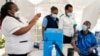 A nurse, left, prepares a shot of AstraZeneca COVID-19 vaccine, manufactured by the Serum Institute of India and provided through the global COVAX initiative, from a portable cold storage box, center, in Machakos, Kenya, March 24, 2021.
