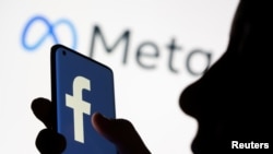 Žena drži pametni telefon sa Fejsbuk logom ispred ekrana novog logoa Meta od 28. oktobra 2021.