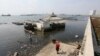 Orang-orang berjalan di dekat tanggul laut raksasa yang digunakan sebagai pembatas untuk mencegah air laut mengalir ke daratan dan menyebabkan banjir di Jakarta, 27 Juli 2019. (Achmad Ibrahim/AP)