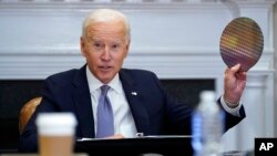 President Joe Biden holds up a silicon wafer as he participates virtually in the CEO Summit on Semiconductor and Supply Chain Resilience in the Roosevelt Room of the White House, April 12, 2021.