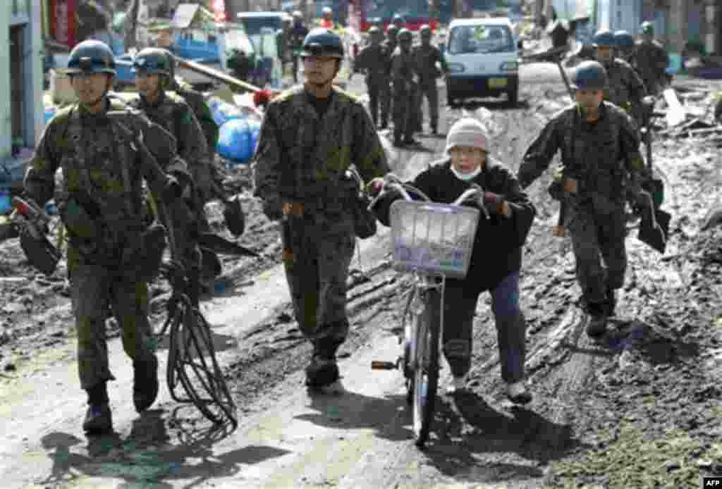 Japan Ground Self-Defense Force soldiers urge an elderly woman to move to higher ground during a tsunami warning Monday, March 14, 2011, in the harbor of Soma city, Fukushima prefecture, Japan, three days after a massive earthquake and tsunami struck the