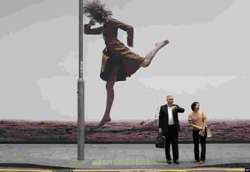 People stand in front of a fashion advertisement along a downtown street in Hong Kong.