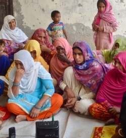 Women in Ferozpur Namak village listen on a narrow caster to a program where victims of domestic violence relate their stories and learn how they faced the challenge. (Anjana Pasricha/VOA)