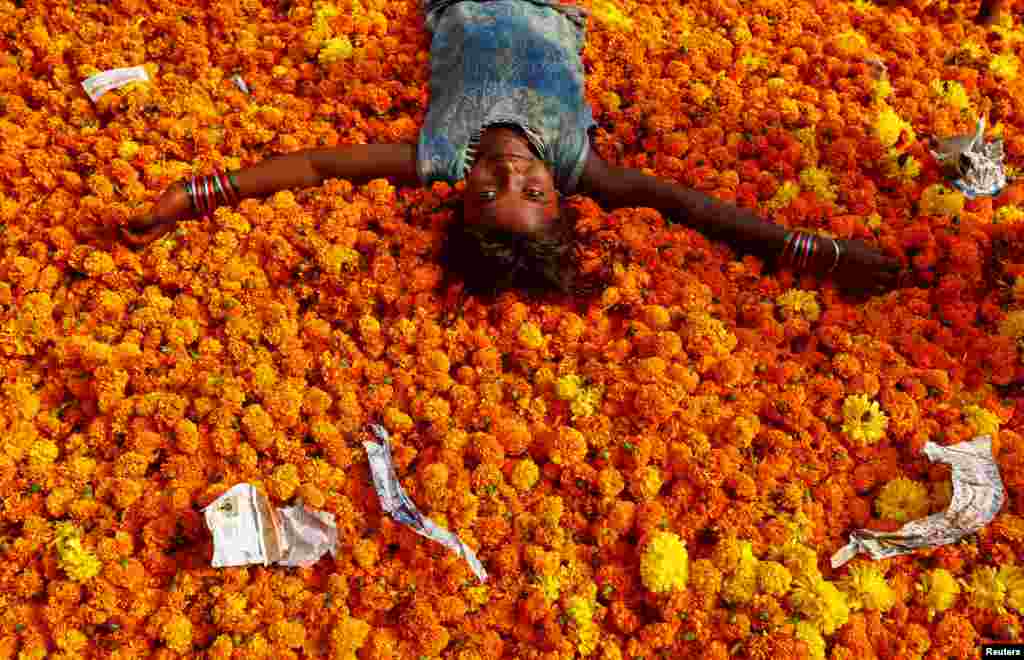 A girl plays on a pile of discarded flowers outside a market, the day after the Diwali celebrations in Mumbai, India.