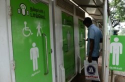 FILE - A man checks his phone as he waits to use a public toilet on a street in Chennai, India, Nov. 15, 2017.