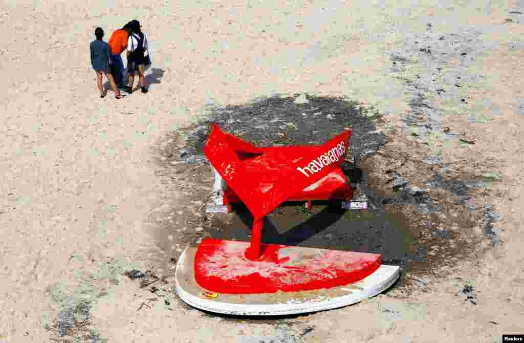 People stand near a sculpture that was damaged due to large waves, during the annual outdoor exhibition known as "Sculpture by the Sea" located on Tamarama Beach in Sydney, Australia.