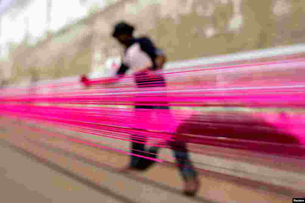 A worker applies color to strings which will be used to fly kites, on a roadside in Ahmedabad, India.