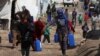 FILE - Syrian refugees walk as they carry containers at a tent settlement in Lebanon's Bekaa Valley, March 12, 2021. 