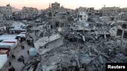 Warga Palestina berjalan di antara puing-puing bangunan, di tengah gencatan senjata antara Israel dan Hamas, di Khan Younis, di Jalur Gaza selatan, 27 Februari 2025. (Foto: Ramadan Abed/Reuters)