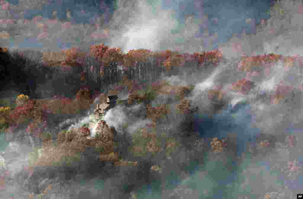 Smoke surrounds a home as seen from aboard a National Guard helicopter near Gatlinburg, Tennessee, Nov. 29, 2016. Thousands of people have fled deadly wildfires that have destroyed hundreds of homes and a resort in the Great Smoky Mountains.