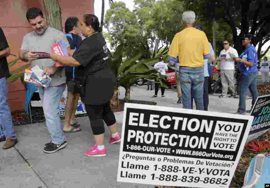 Ingrid Vaca, of Falls Church, Virginia, a volunteer with Election Protection, second from left, hands a voter a leaflet informing him about voter's rights, outside of a polling station at the Miami-Dade County Auditorium, in Miami, Florida.